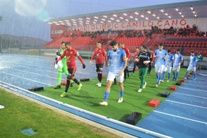 Los dos equipos saltando al césped del Estadi Olímpic Camilo Cano bajo una fuerte lluvia