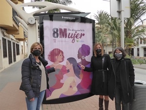Cari Rodríguez, técnica Igualdad, Gemma Márquez, cocnejala Igualdad y Mª Jesús Jumilla, concejala de Juventud junto a una marquesina con el cartel "Día Internacional de la Mujer"
